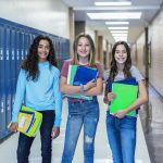 Group of Junior High school Students standing together in a school hallway. Female classmates smiling and having fun together during a break at school