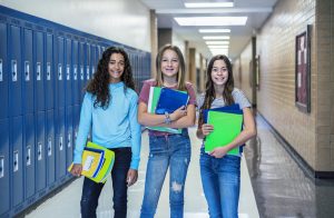 Group of Junior High school Students standing together in a school hallway. Female classmates smiling and having fun together during a break at school